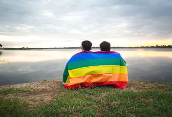 Two people wearing pride flag looking at lake