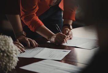 People leaning over table and writing on paper
